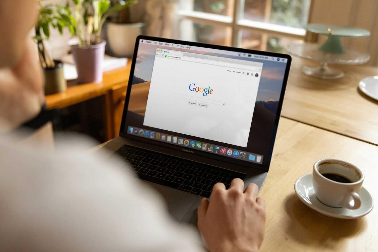 Nutzung von Google auf einem MacBook neben einer Kaffeetasse.