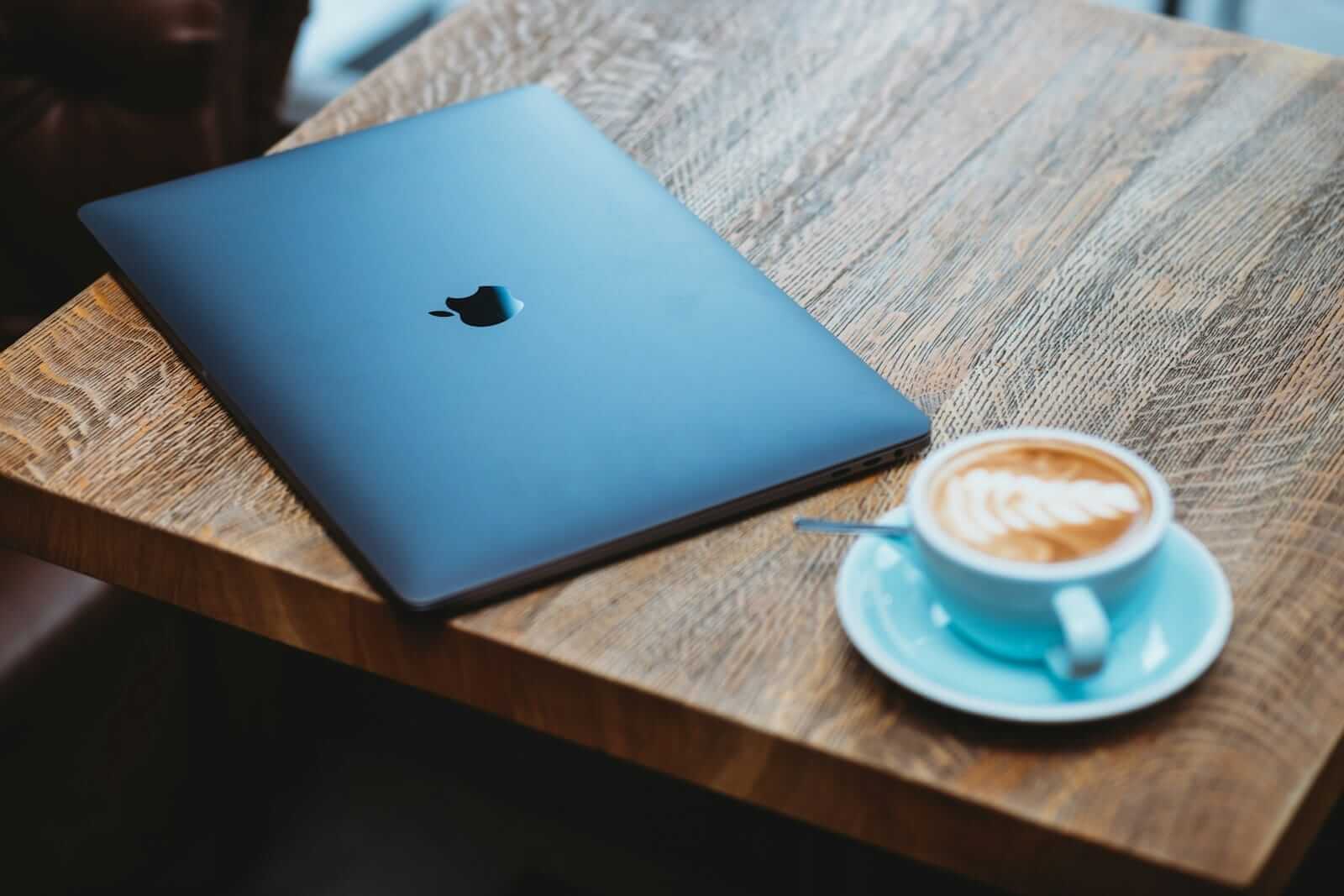 Geschlossenes Laptop neben Kaffeetasse auf Holztisch.